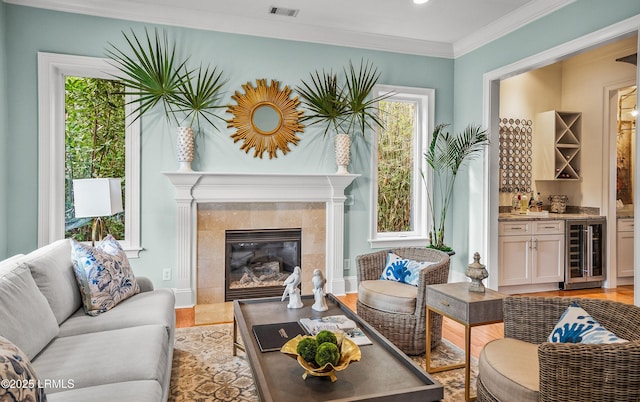 living area featuring a dry bar, visible vents, light wood-style flooring, wine cooler, and ornamental molding