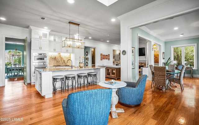 interior space featuring a warm lit fireplace, visible vents, a chandelier, and light wood-style floors