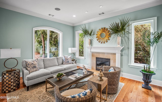 living room featuring light wood-style flooring, ornamental molding, baseboards, and a tile fireplace