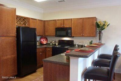 kitchen with black appliances, a kitchen bar, ornamental molding, kitchen peninsula, and light wood-type flooring