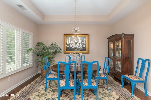 dining area with hardwood / wood-style floors, a raised ceiling, and a chandelier