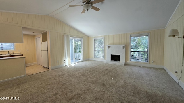 unfurnished living room with a sink, light colored carpet, a brick fireplace, ceiling fan, and vaulted ceiling