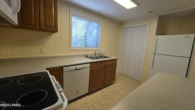 kitchen featuring brown cabinetry, light countertops, light tile patterned flooring, white appliances, and a sink