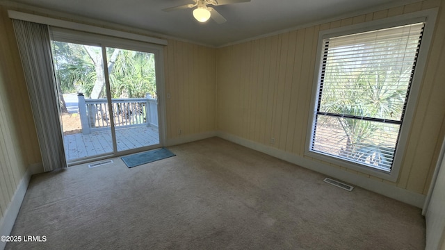 carpeted empty room featuring a wealth of natural light, visible vents, a ceiling fan, and ornamental molding