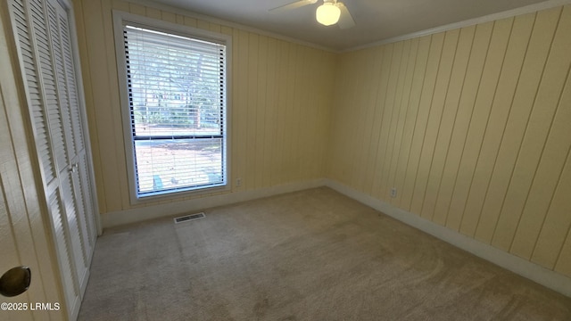 carpeted empty room with ceiling fan, visible vents, and ornamental molding