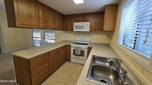 kitchen featuring white appliances, light tile patterned floors, a peninsula, a sink, and light countertops