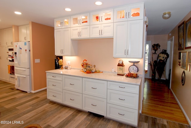 kitchen featuring white cabinetry, light stone countertops, hardwood / wood-style floors, and white appliances