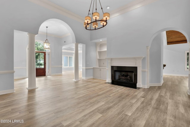 unfurnished living room with ornate columns, ornamental molding, light wood-type flooring, and built in shelves