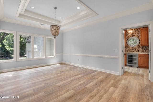 spare room with a raised ceiling, ornamental molding, a notable chandelier, and beverage cooler