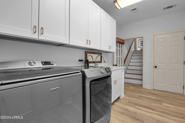 laundry room featuring cabinets, sink, washer and dryer, and light wood-type flooring