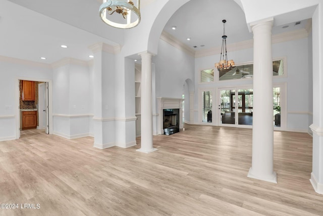 unfurnished living room with light hardwood / wood-style flooring, a towering ceiling, decorative columns, ornamental molding, and a chandelier