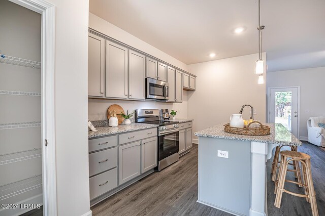 kitchen with dark wood-type flooring, gray cabinetry, a center island with sink, appliances with stainless steel finishes, and pendant lighting