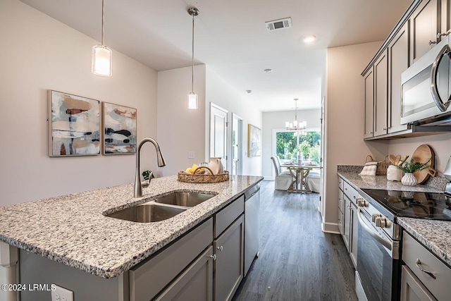 kitchen featuring dark wood-type flooring, sink, an island with sink, stainless steel appliances, and light stone countertops