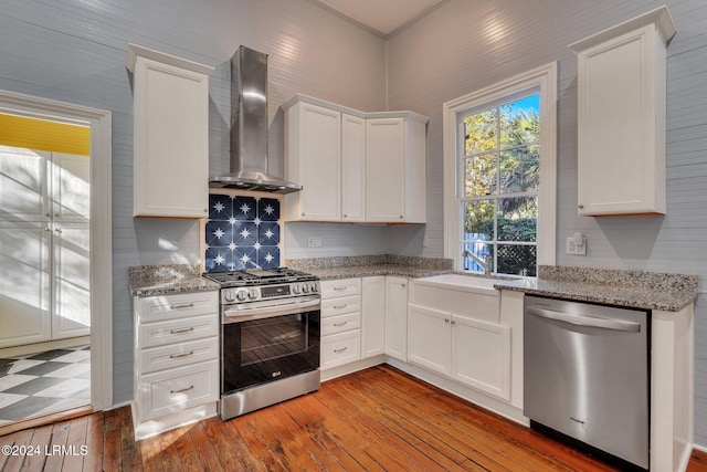 kitchen featuring wall chimney range hood, light wood-type flooring, white cabinets, and appliances with stainless steel finishes