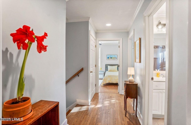 hallway featuring crown molding, baseboards, an upstairs landing, and light wood-style floors