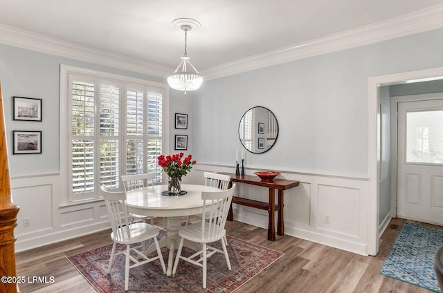 dining room with a wainscoted wall, ornamental molding, wood finished floors, a chandelier, and a decorative wall