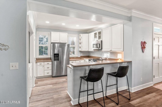 kitchen featuring light wood-type flooring, a peninsula, appliances with stainless steel finishes, and a breakfast bar