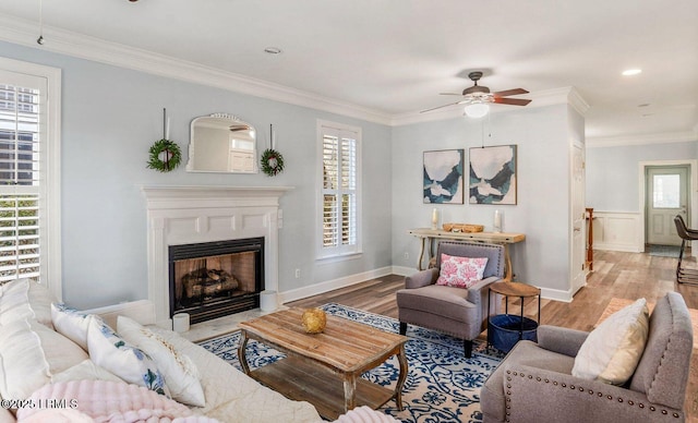 living area with a fireplace with flush hearth, ceiling fan, wood finished floors, and crown molding