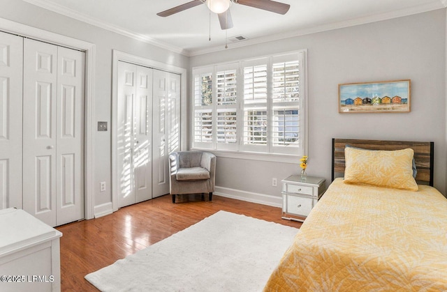 bedroom with multiple closets, ornamental molding, baseboards, and wood finished floors