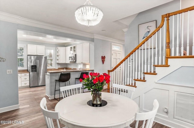 dining area with crown molding, light wood finished floors, an inviting chandelier, and stairs