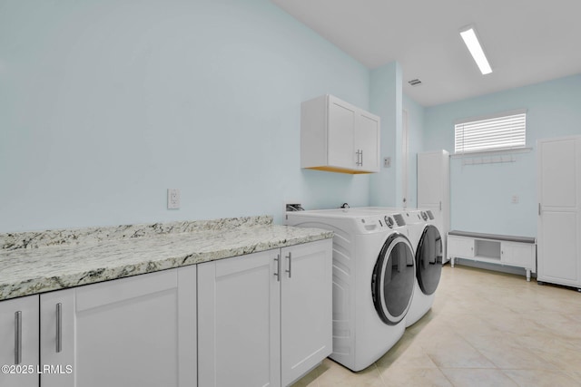 clothes washing area featuring cabinets, light tile patterned flooring, and washing machine and clothes dryer