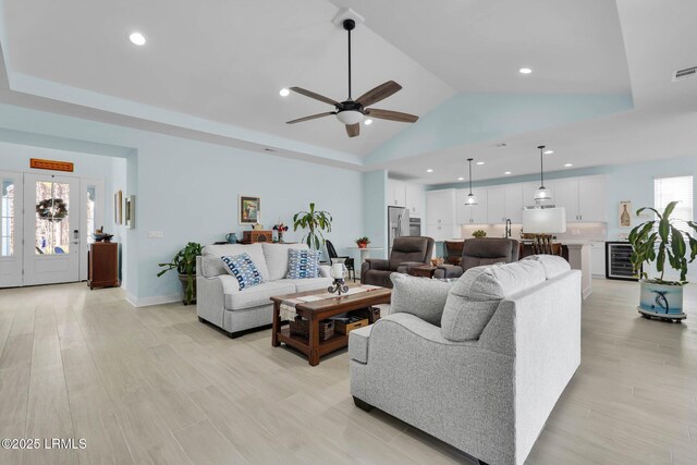 living room with wine cooler, ceiling fan, a raised ceiling, and light wood-type flooring