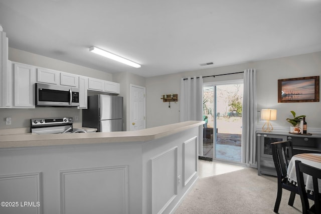 kitchen with stainless steel appliances, light colored carpet, white cabinets, and kitchen peninsula