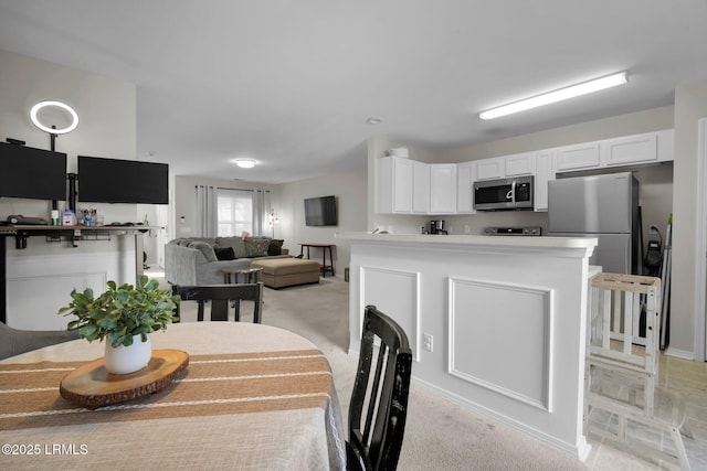 kitchen with appliances with stainless steel finishes, light colored carpet, and white cabinets