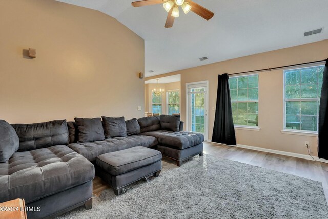 living room featuring ceiling fan with notable chandelier, wood-type flooring, and vaulted ceiling