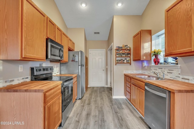 kitchen featuring butcher block counters, sink, light wood-type flooring, stainless steel appliances, and a textured ceiling