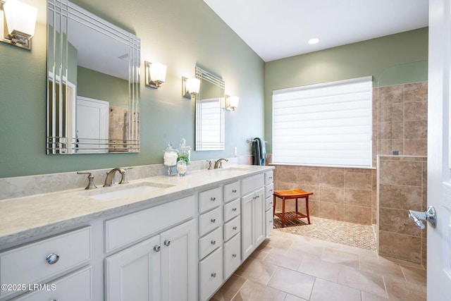 bathroom with double vanity, tiled shower, a sink, and tile patterned floors