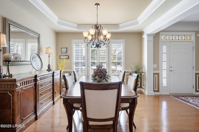 dining area featuring a notable chandelier, ornamental molding, light wood-type flooring, a tray ceiling, and ornate columns