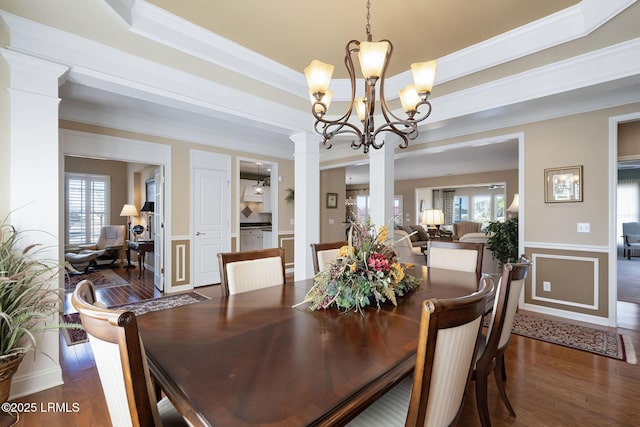 dining area with decorative columns, ornamental molding, wood finished floors, a tray ceiling, and a notable chandelier