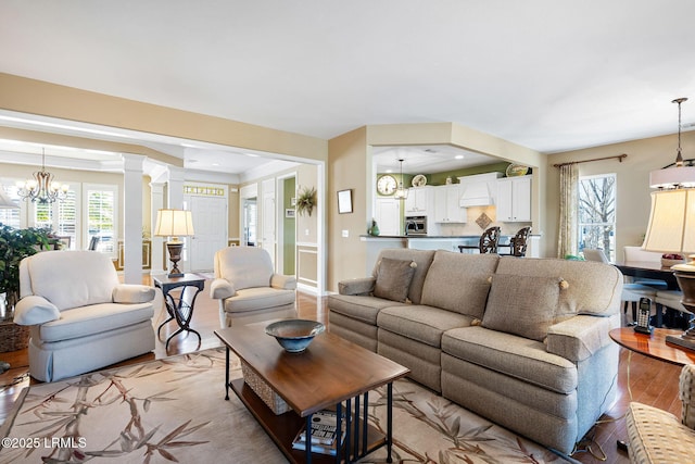 living area with light wood finished floors, recessed lighting, decorative columns, and a notable chandelier