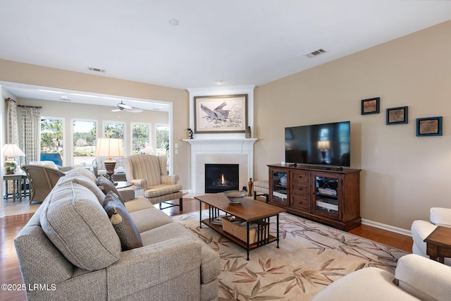 living area featuring a warm lit fireplace, light wood-type flooring, visible vents, and baseboards