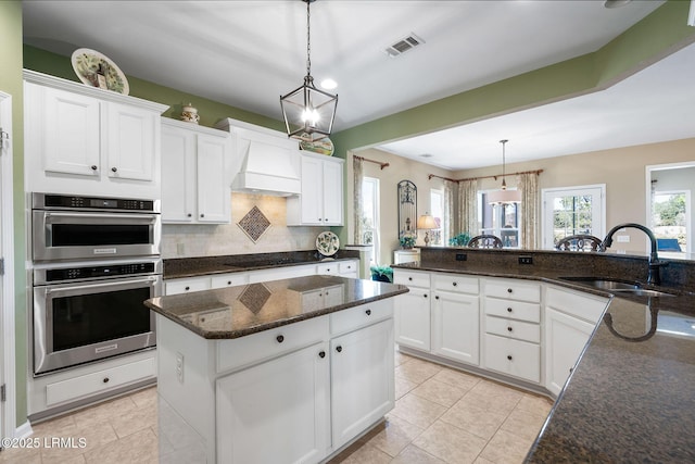 kitchen featuring white cabinets, custom range hood, a center island, double oven, and a sink