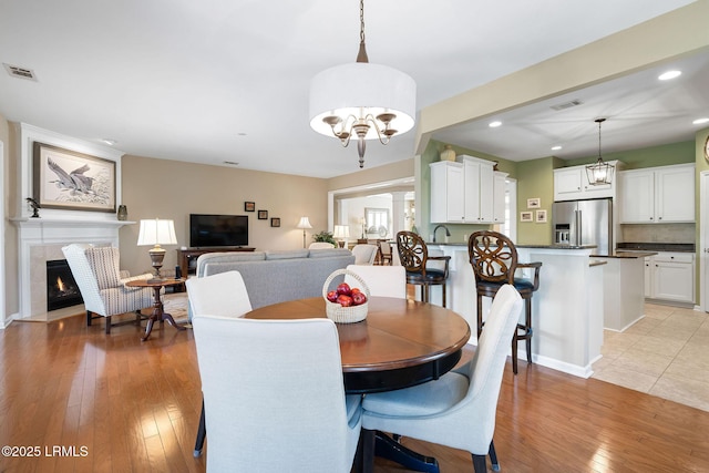 dining room with a lit fireplace, light wood-style floors, visible vents, and an inviting chandelier