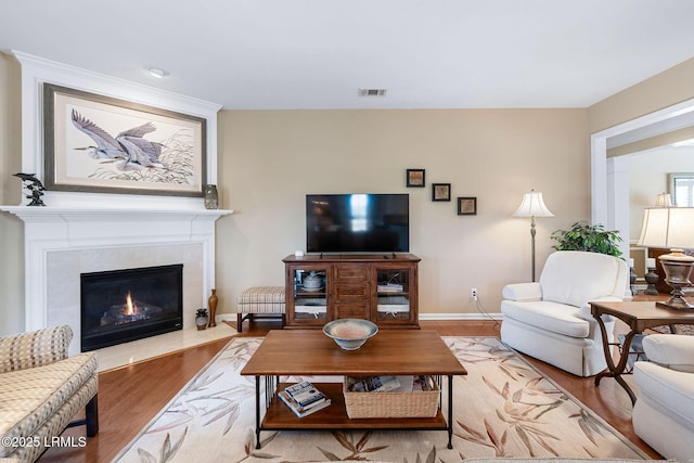 living area featuring a tile fireplace, wood finished floors, visible vents, and baseboards