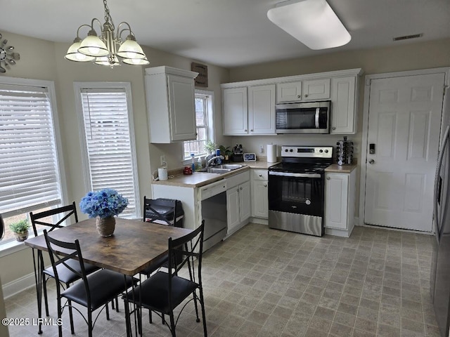 kitchen featuring appliances with stainless steel finishes, decorative light fixtures, sink, white cabinetry, and an inviting chandelier