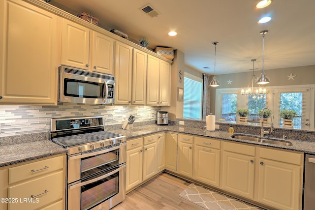 kitchen with sink, dark stone countertops, decorative backsplash, hanging light fixtures, and stainless steel appliances