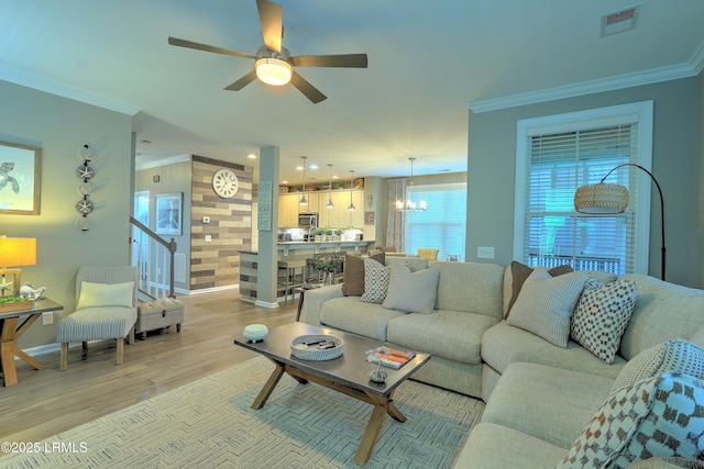 living room with ornamental molding, ceiling fan with notable chandelier, and light wood-type flooring