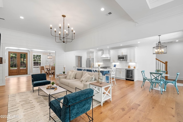 living room with light wood-style floors, beverage cooler, a chandelier, visible vents, and ornamental molding