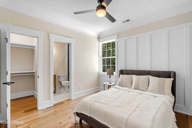 bedroom with visible vents, baseboards, a spacious closet, ornamental molding, and light wood-style flooring