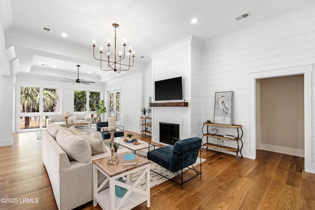 living area with visible vents, a fireplace, wood finished floors, ceiling fan with notable chandelier, and ornamental molding