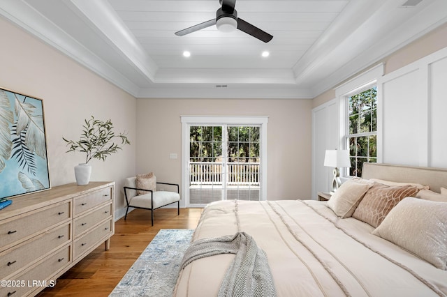 bedroom with access to outside, multiple windows, wood finished floors, and a raised ceiling