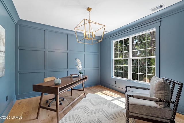 office featuring light wood-style floors, a decorative wall, a chandelier, and visible vents