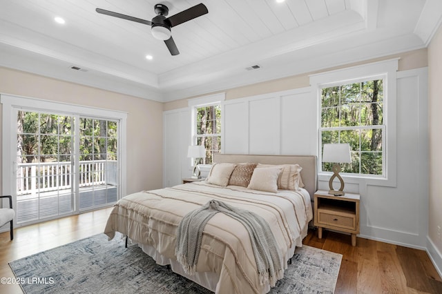 bedroom with access to outside, a tray ceiling, multiple windows, and visible vents