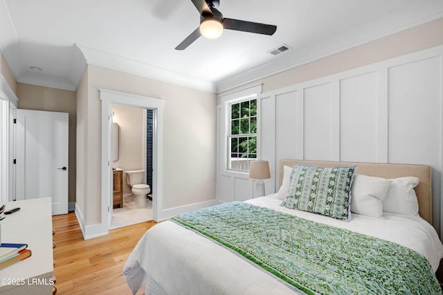 bedroom with visible vents, baseboards, light wood-style floors, ornamental molding, and ensuite bath