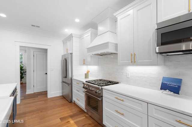 kitchen featuring white cabinetry, premium appliances, light wood-style floors, and tasteful backsplash