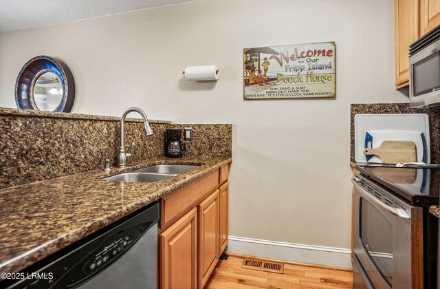 kitchen featuring stainless steel appliances, sink, light hardwood / wood-style flooring, and dark stone countertops